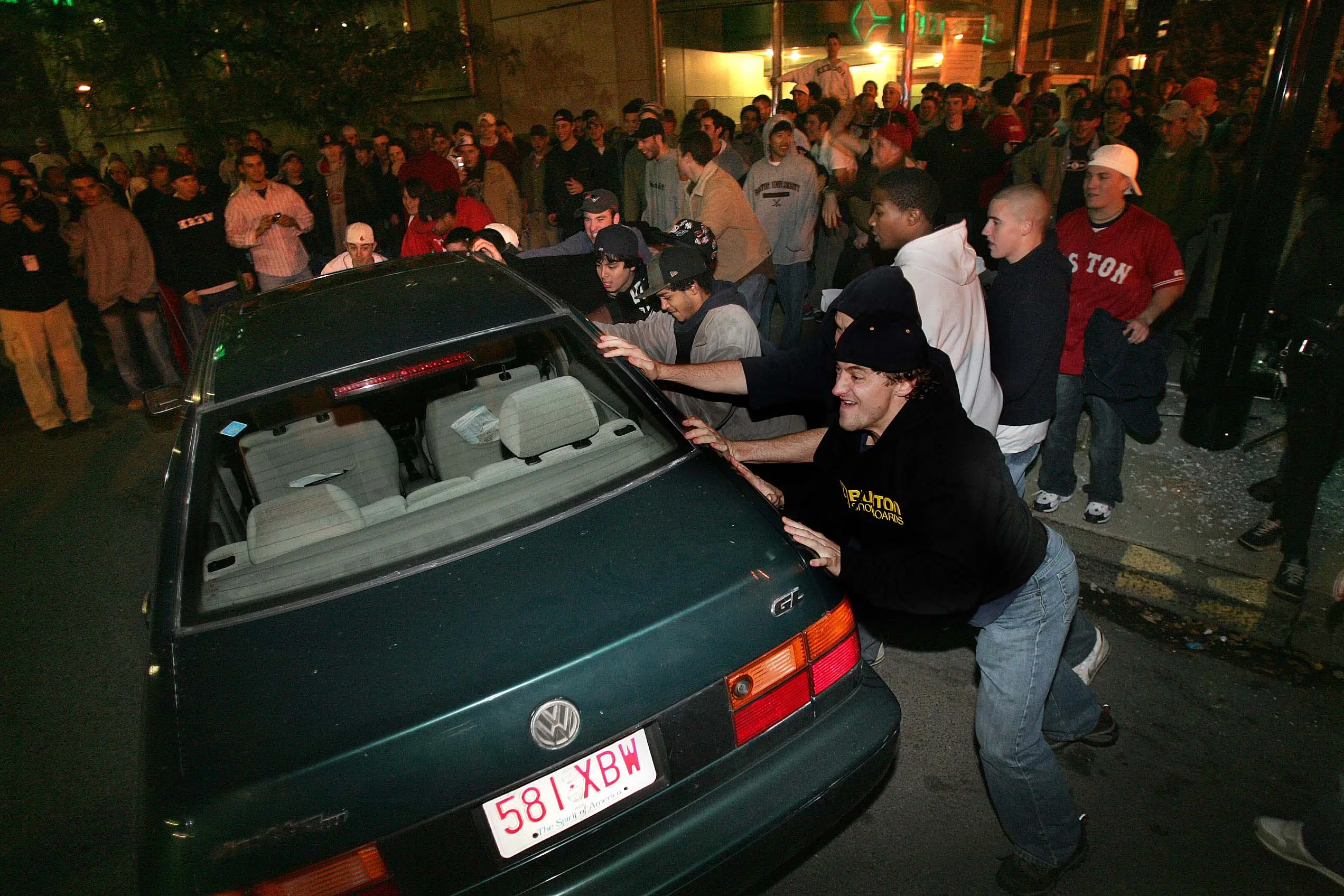 A group of men attempt to roll over a car in Kenmore Square after the Red Sox victory.