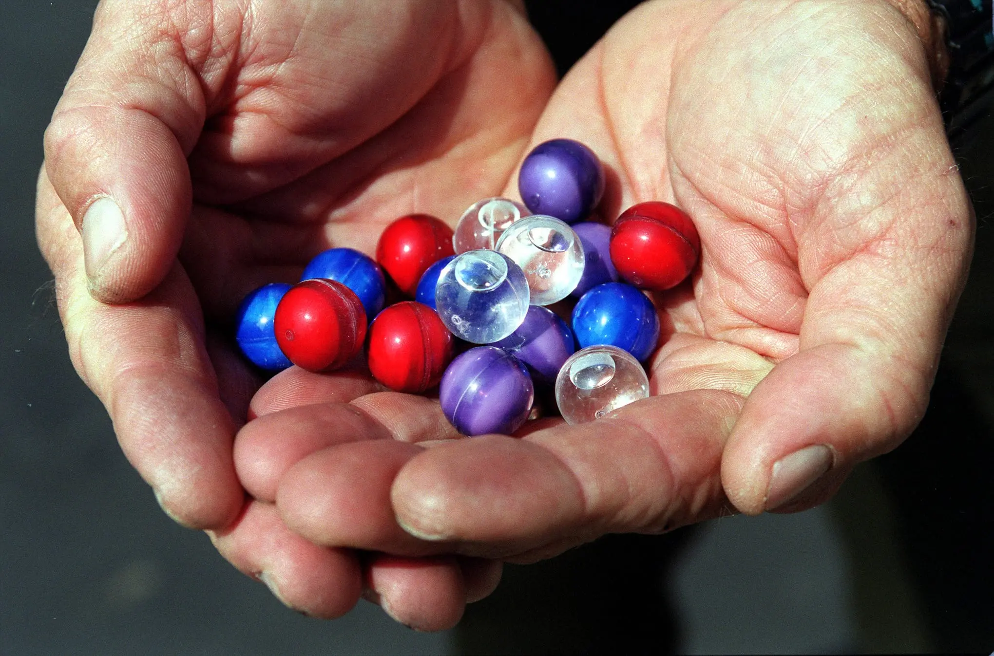 A pair of hands hold a pile of small colorful spheres.