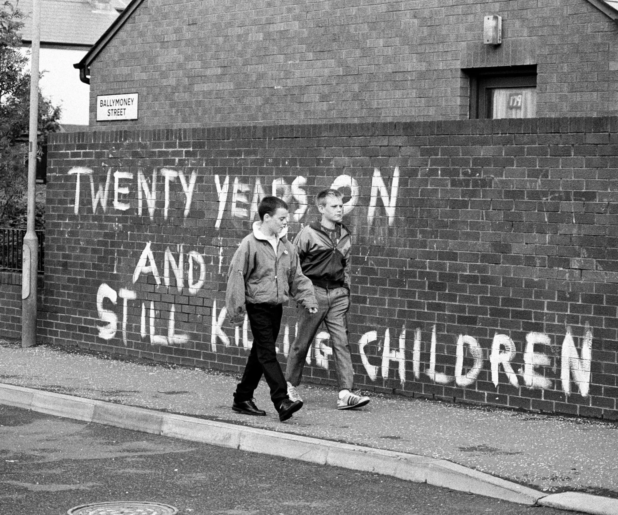 Two boys walk past the wall with the painted slogan "Twenty years on and still killing our children" on Ballymoney Street in Belfast in 1989.