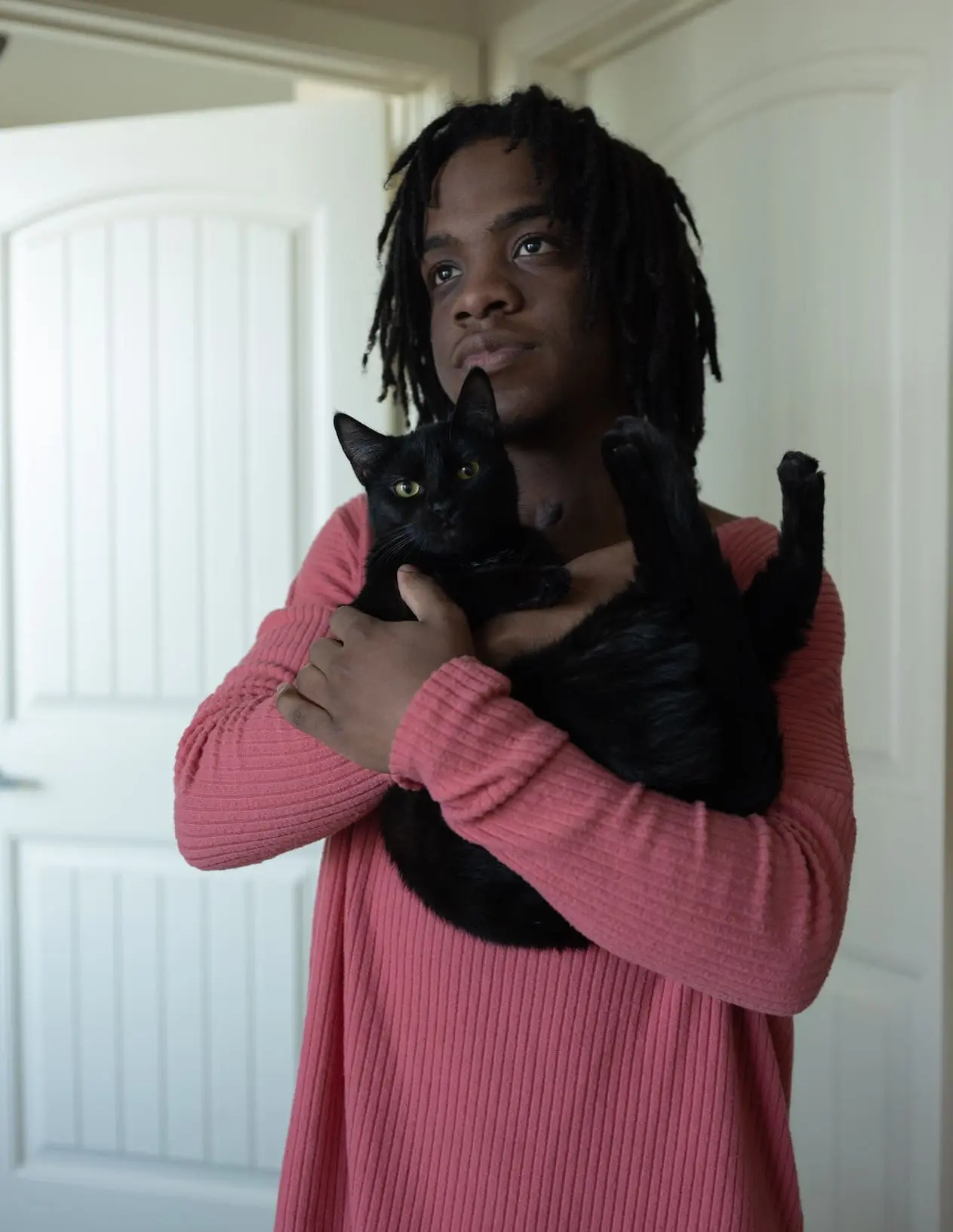 A person in a pink shirt stands, holding a black cat.