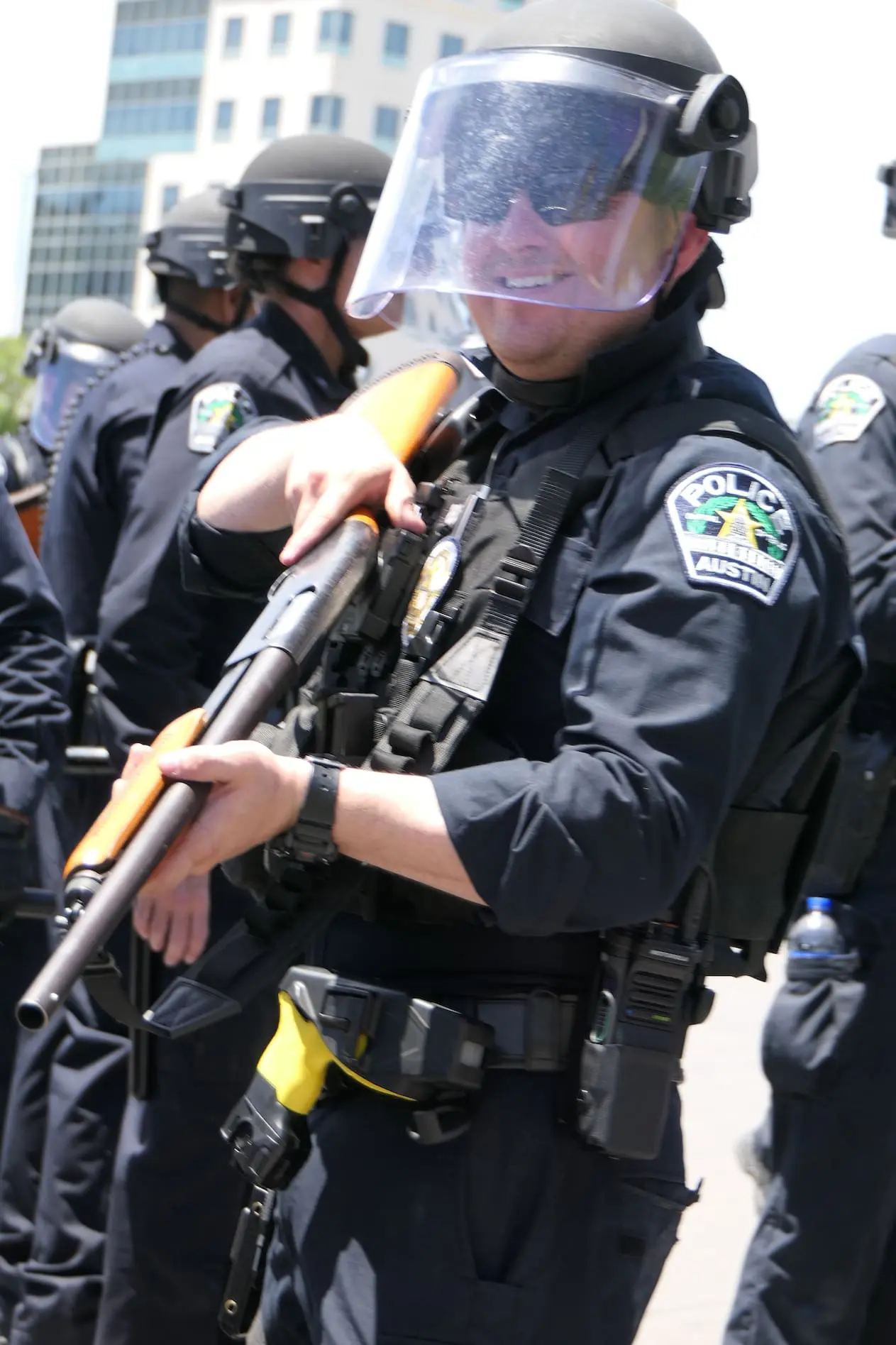 An Austin Police officer smells while holding a shotgun in a crowd of other officers.
